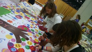 Fiona, Camille, and Katie paint mural boards in the COBO Center
